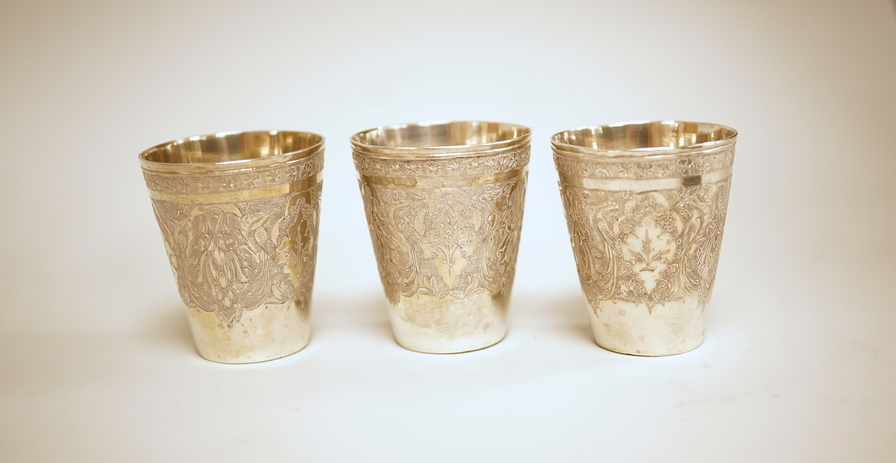 A set of six 20th century Middle Eastern white metal tots, 42mm and matching tray, 25.2cm, all engraved with geometric foliate decoration.